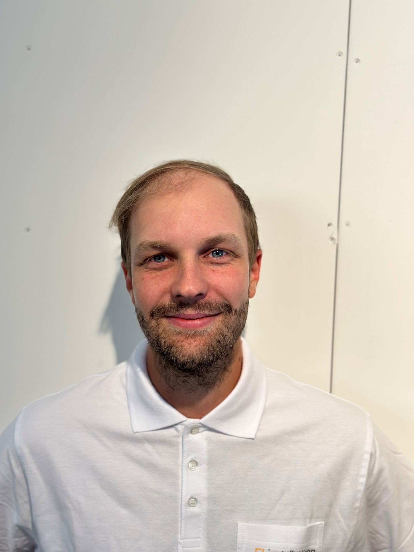 Person wearing a white collared shirt against a plain wall.