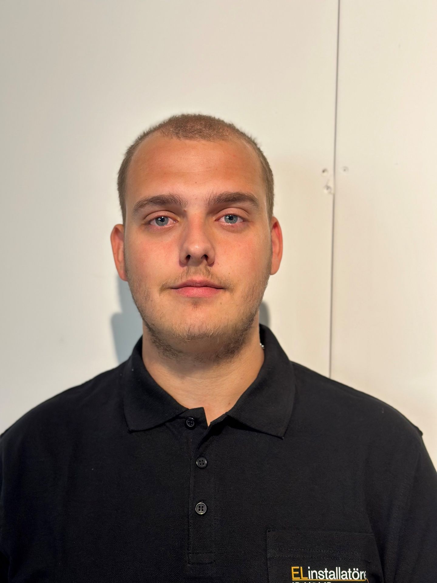 Person in a black polo shirt with embroidered logo, posed against a plain wall.