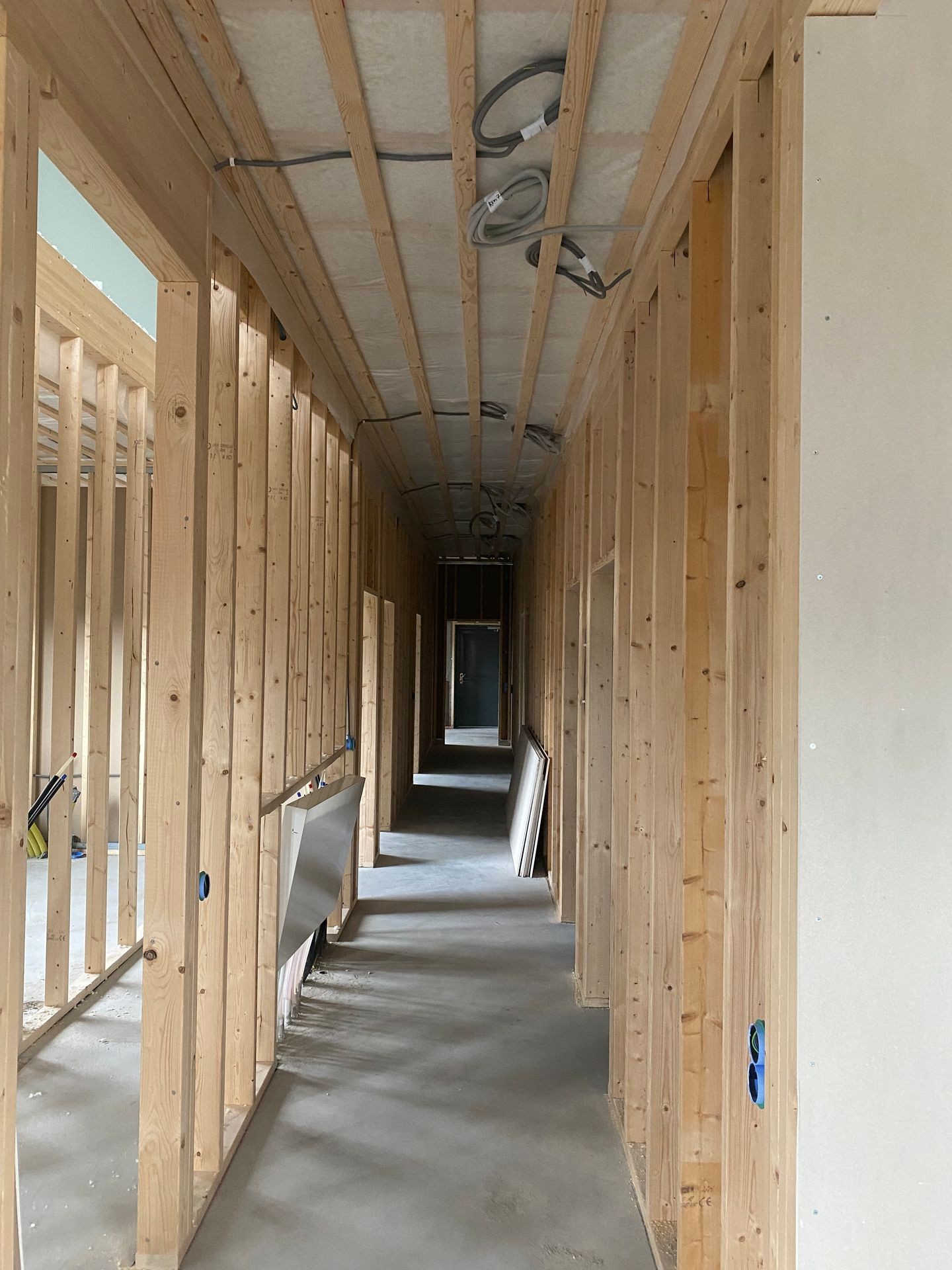 Interior view of a building under construction with exposed wooden frames and electrical wiring visible on the ceiling.