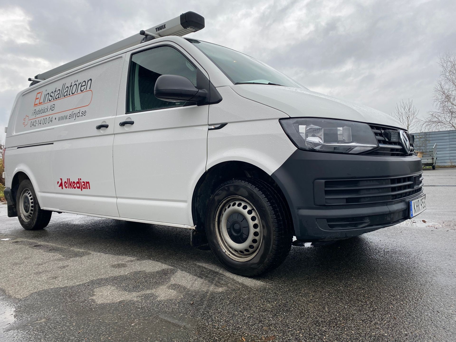 White service van with company branding parked on a wet road under an overcast sky.